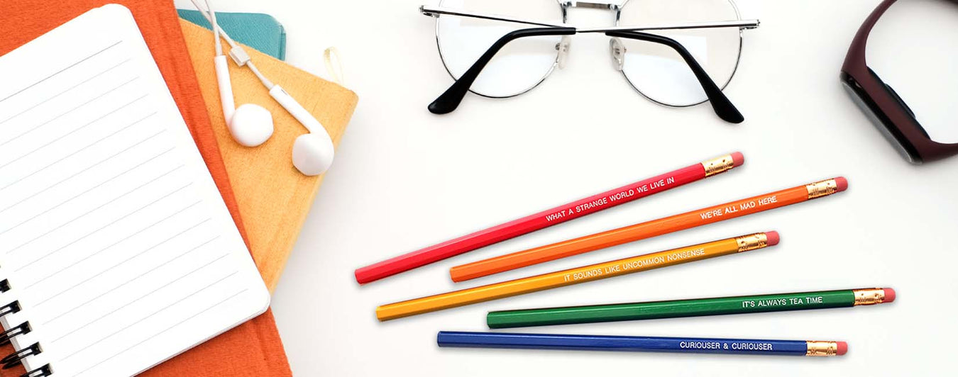 rainbow colored alice in wonderland pencils flatlay with notebook and glasses
